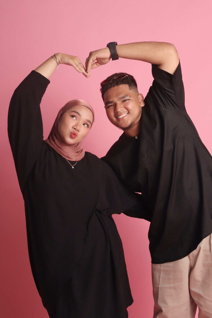 Lovely Malay couple photo doing a big heart shape gesture with a pink background