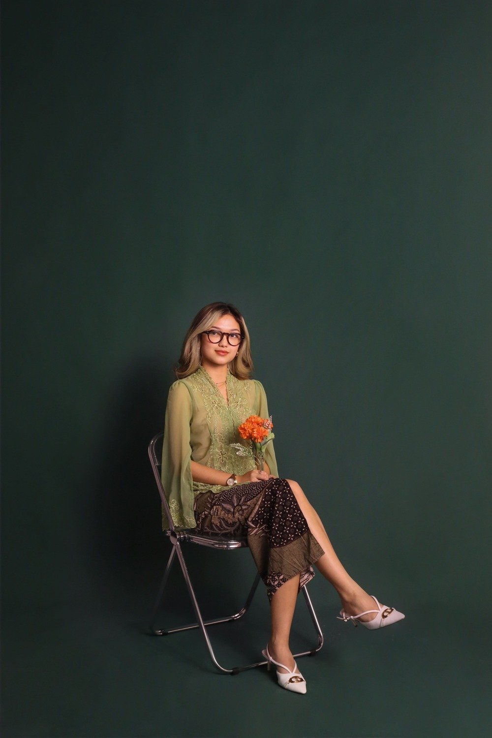 Woman portrait sit flower on hand with traditional clothes with dark green background in photo studio